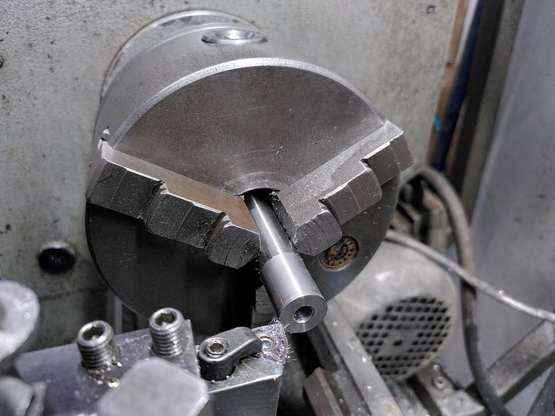 A bar of steel held in the 3 jar chuck of a lathe. It has a hole drilled
in the end, and the end 30mm or so has been machined to have a different
finish to the rest. There's a carbide insert tool to the left of the
chuck.