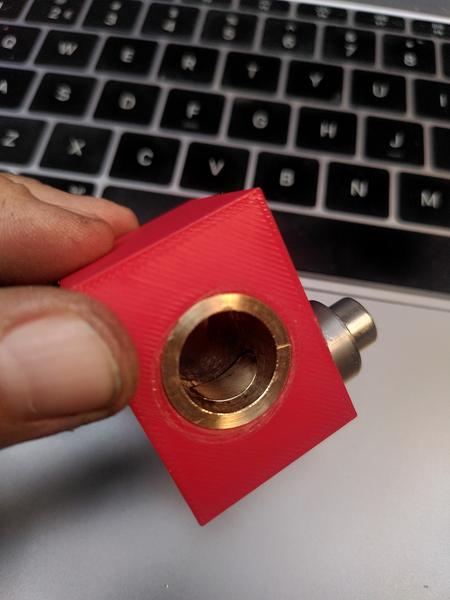 A block of red PLA with a bronze sleeve inserted. Inside the bronze
sleeve there's a brass part just visible with scalloped curve taken out of
it. On top of the PLA block a fat steel washer is held in palce with a
stainless steel cap head bolt.